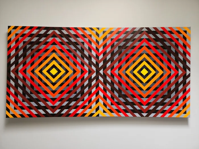 Wide canvas painted with two large concentric diamonds in red, orange and yellow set against grey and black chevrons.