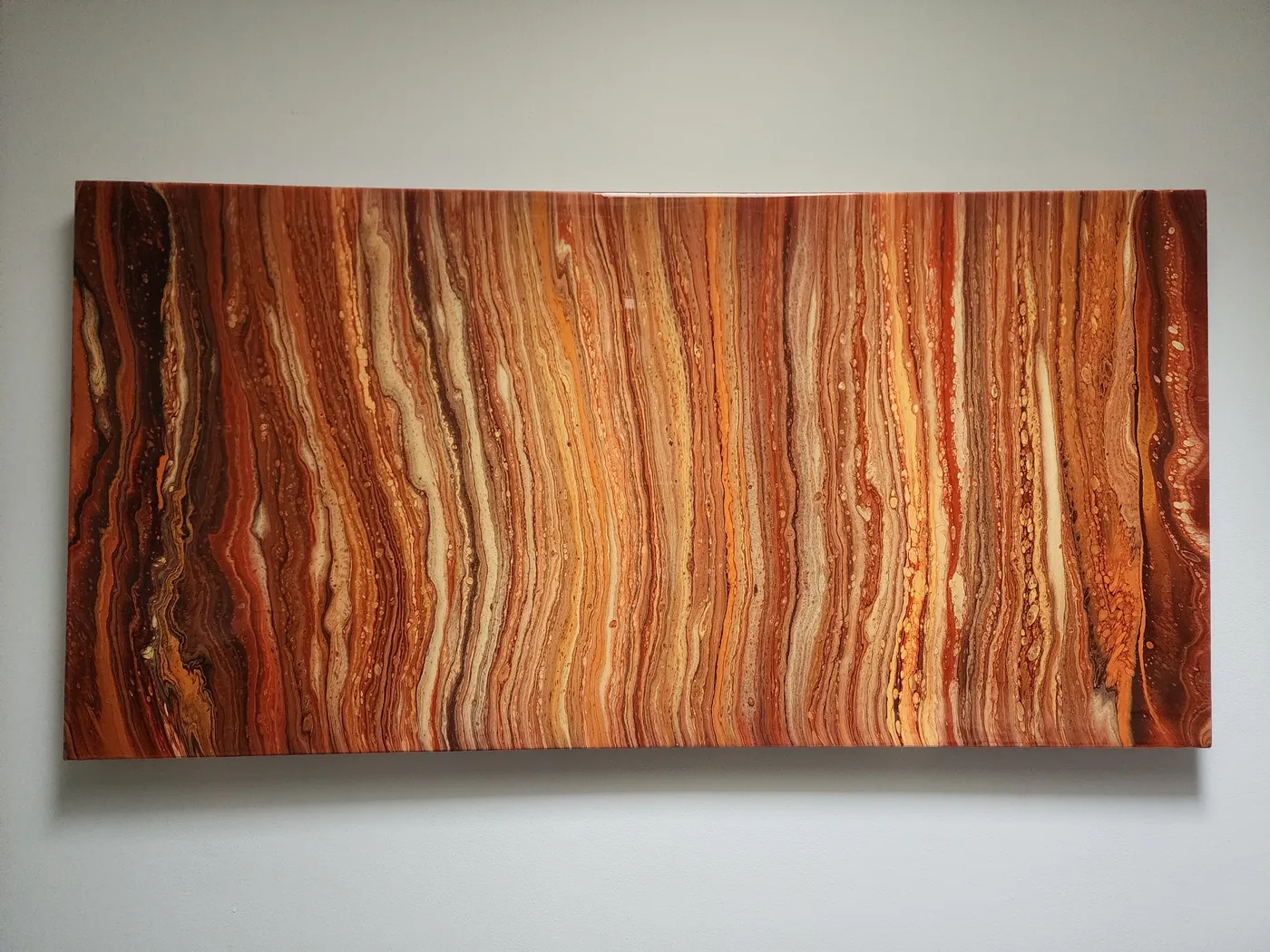 A large canvas painting mounted to a neutral wall. The painting is a fluid art piece in stunning reds, oranges, and tans, giving the look of the planet Jupitor or Mars.