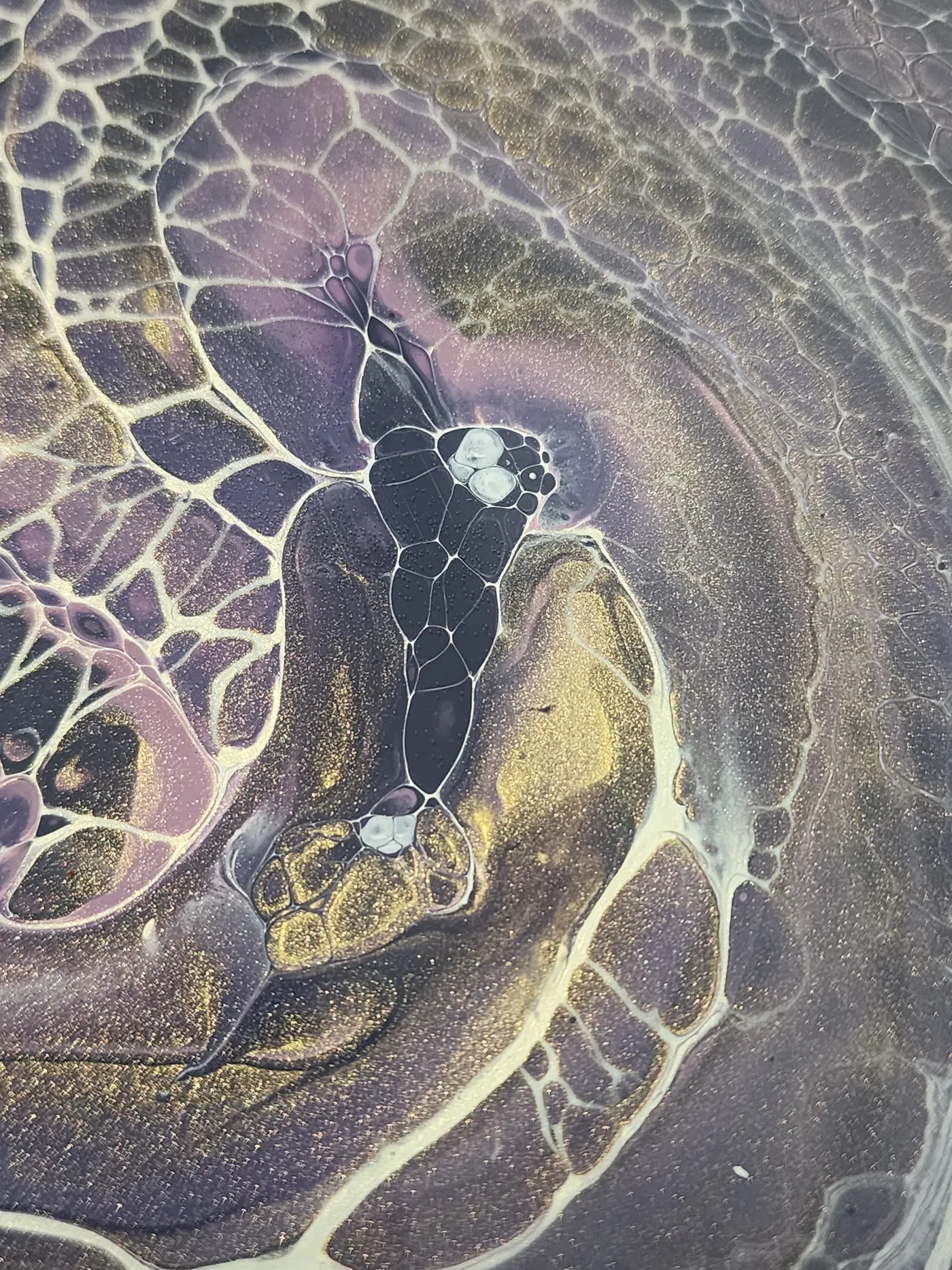 An up-close photo of the center of the art piece with swirling gold, gray, and purple paint with metallic flecks.