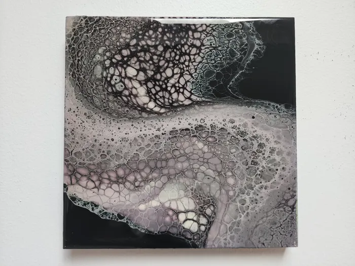 A small, square fluid art piece on a neutral wall. The piece shows off a wave of pale lavender and gray fluid cells over a black base.