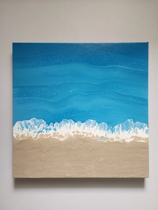 A square canvas fluid painting of a seascape from above. The piece has a striking blue ocean with foaming waves where it meets the beach made of real sand on canvas.