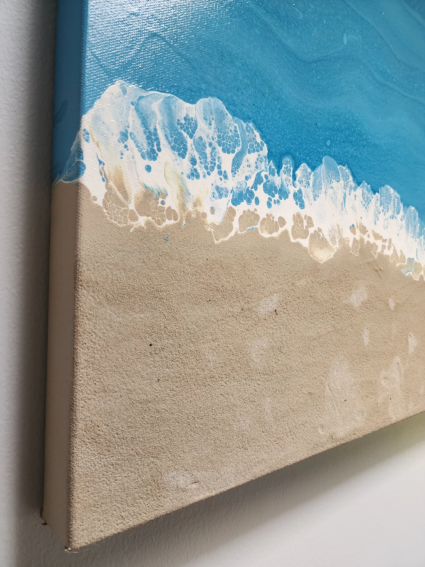 AN angled viewAn angled view of the seascape art piece showcasing the art, including the sand, wrapping the edges of the canvas.
