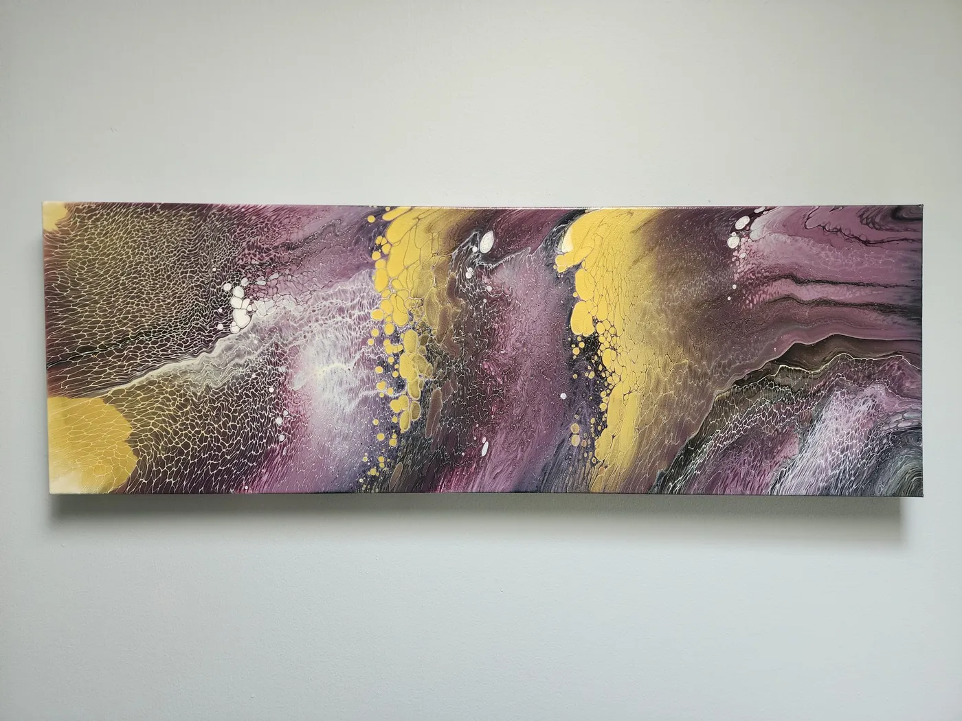 A wide, fluid art, canvas painting on a neutral wall. The piece shows off alternating golden and violet ribbons with areas of white and grays visible.