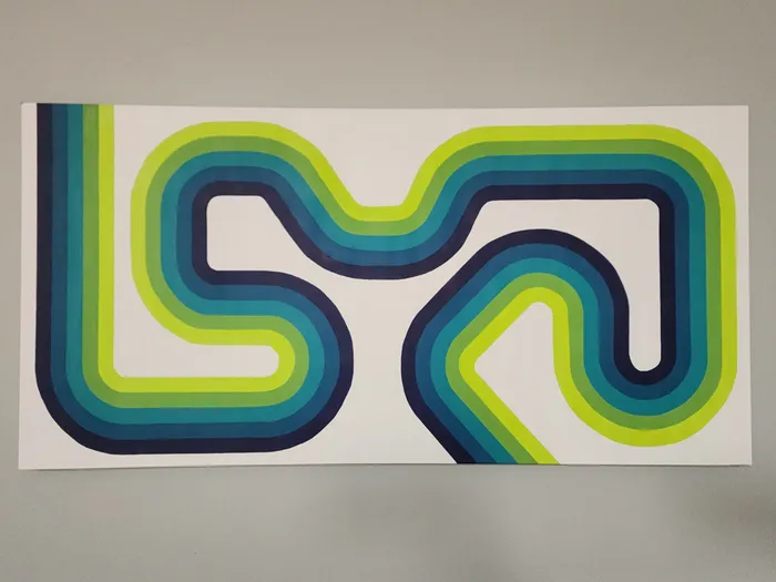 An abstract art piece on a neutral wall. The piece showcases an abstract path shape running left-to-right with the path being a five-line, hard-edge gradient from navy blue to a bright yellow-green.