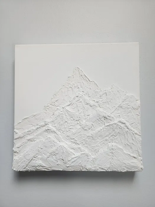 An unpainted, white canvas piece on a neutral wall. The piece is a textured art piece made of plaster depicting layered mountain peaks.