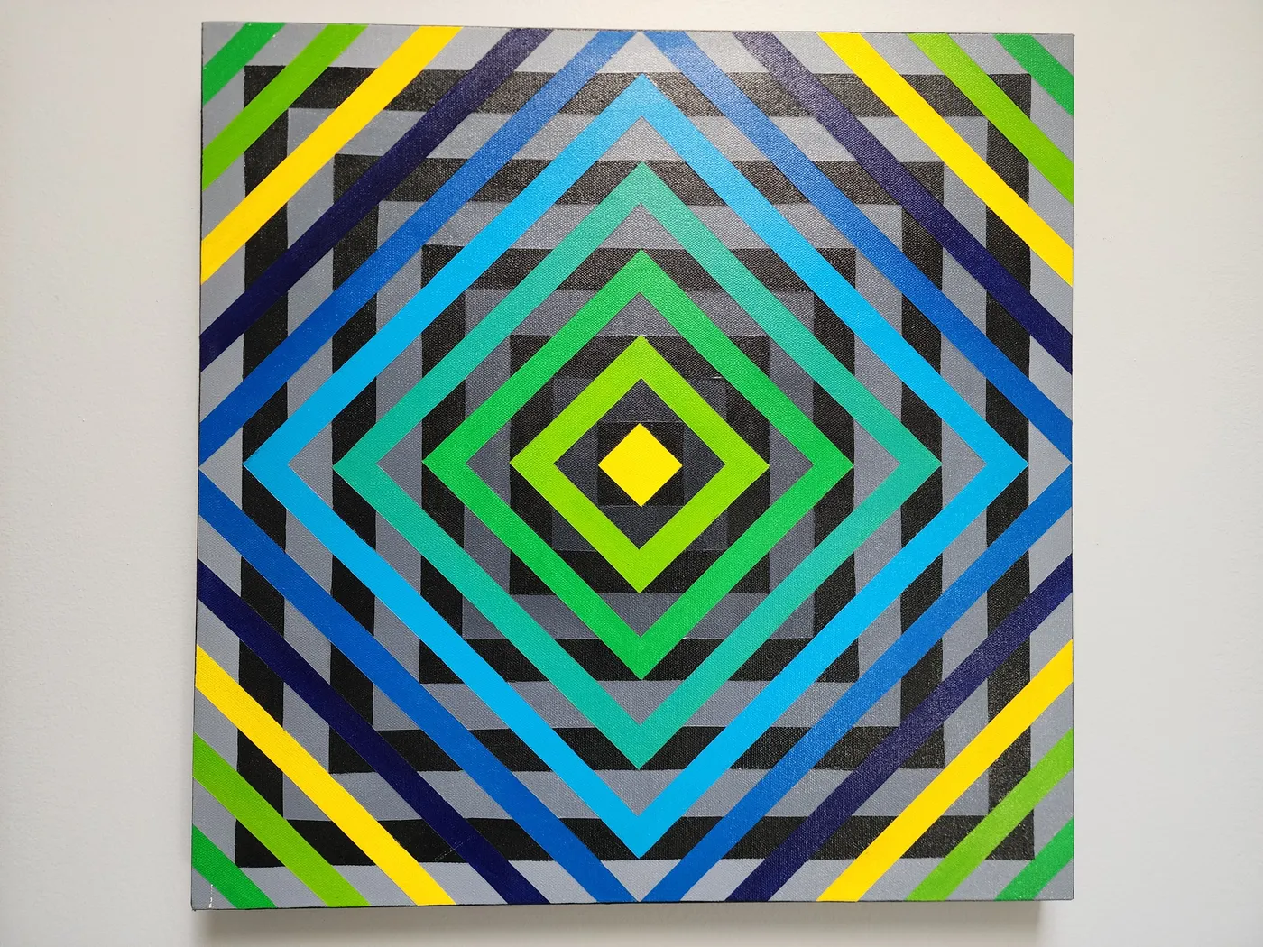 An abstract art piece on a neutral wall. The piece depicts a base of patterned gray and black squares overlayed with a 90 degree rotated set of squares in a stunning gradient from bright yellow at the center to navy blue at the edge, passing through stunning greens, teals, and blues.