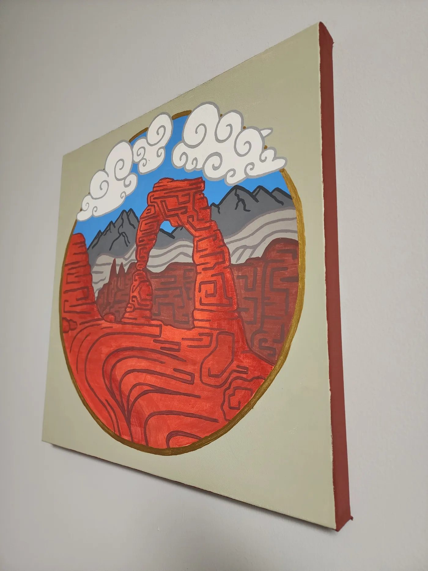 Looking at an angle to a canvas painting of Delicate Arch in Arches National Park hanging on a neutral colored wall. The angle shows off the painted canvas edges.