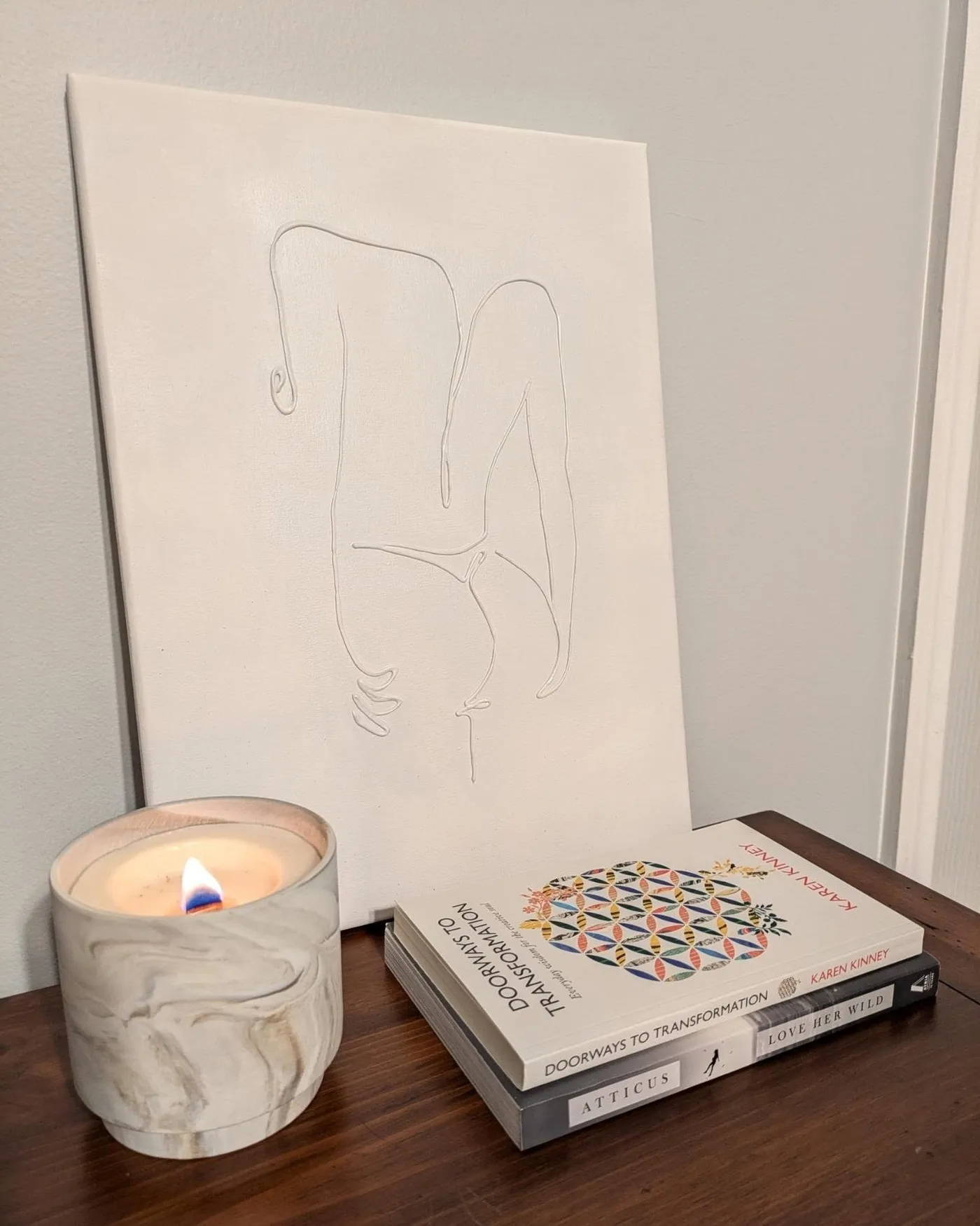 The relief canvas propped on a wood table beside a lit candle and a stack of books.