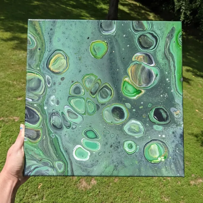 Square canvas held up over grass, acrylic poured in deep green with pale cells ringed in gold and white.