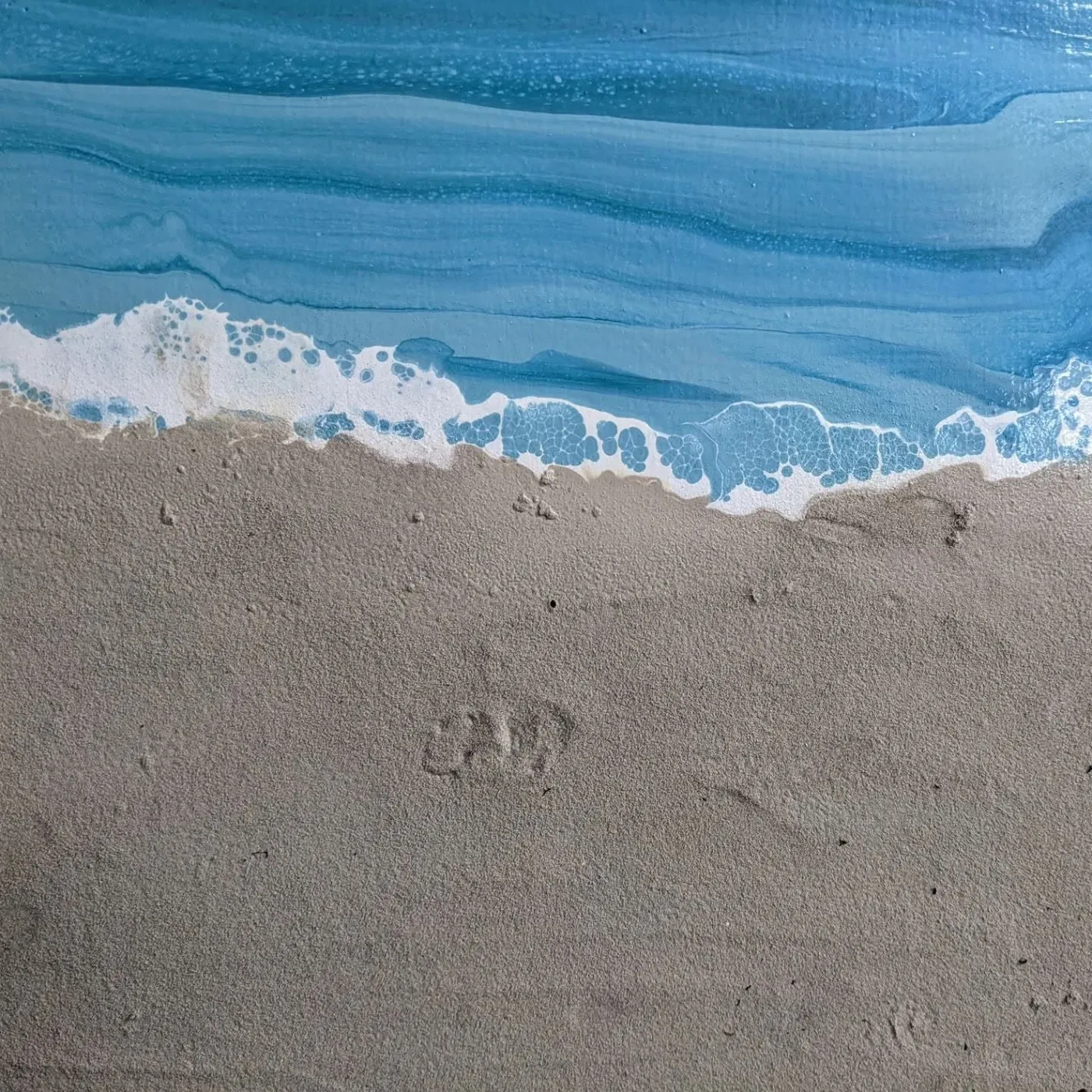 Detail of the shoreline with small footprints pressed into the sand.